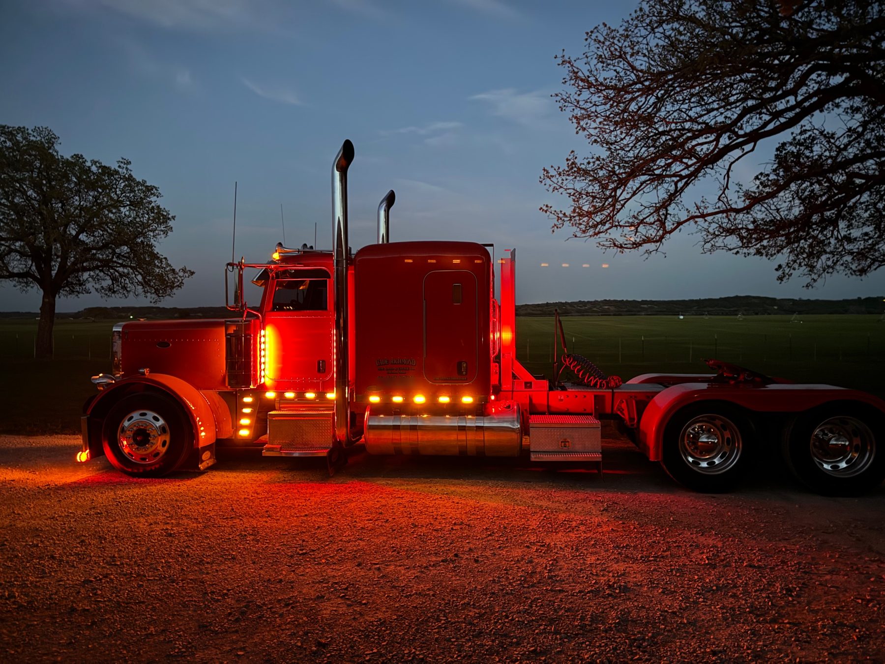 Red Peterbilt truck lettered Cade Richmond Hay, Land & Cattle at dusk