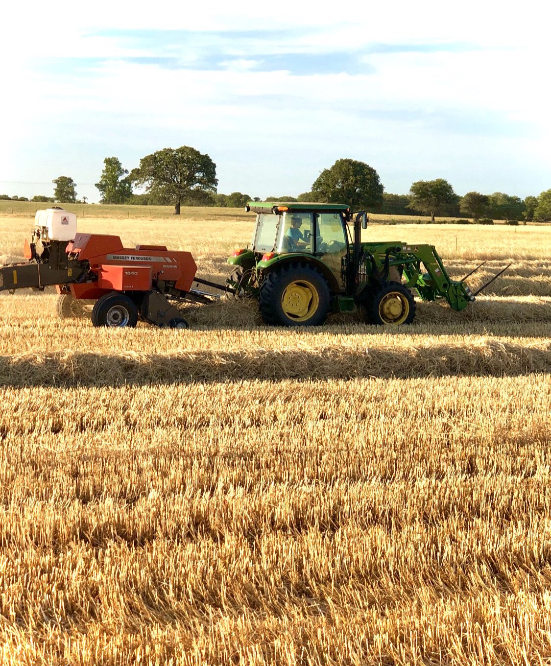 John Deere tractor pulling a Massey Ferguson square baler through a field of straw