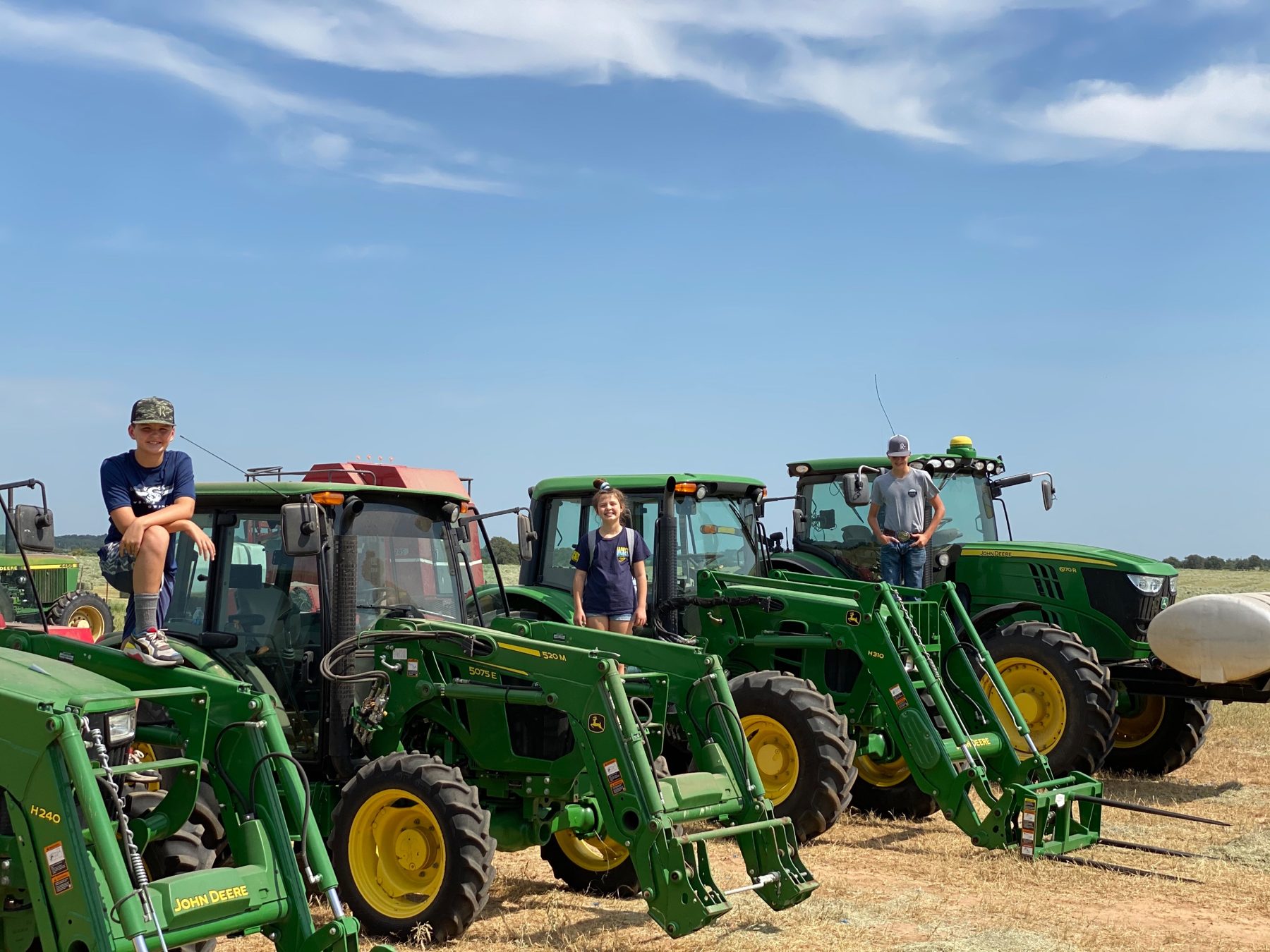 The three Richmond kids standing on a lineup of John Deere tractors